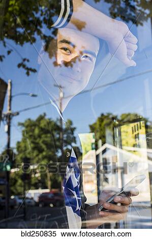 Stock Photography - Smiling Chinese man leaning on window holding cell phone. Fotosearch