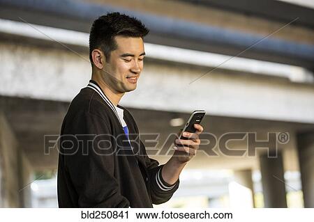 Stock Image - Smiling Chinese man texting on cell phone. Fotosearch