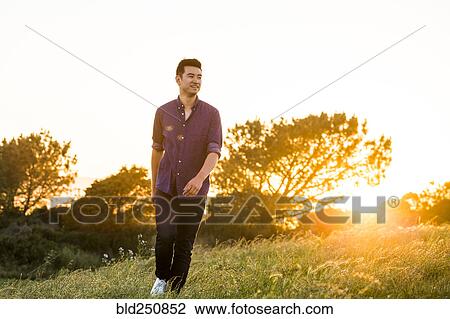 Stock Image - Smiling Chinese man walking on hill. Fotosearch