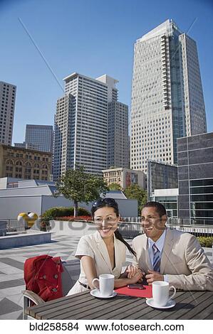 Picture - Smiling couple holding hands and drinking coffee outdoors. Fotosearch