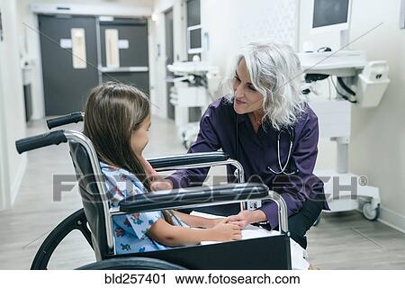 Stock Image - Smiling doctor talking to girl in wheelchair. Fotosearch