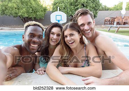 Stock Photo - Smiling friends in swimming pool posing for selfie. Fotosearch