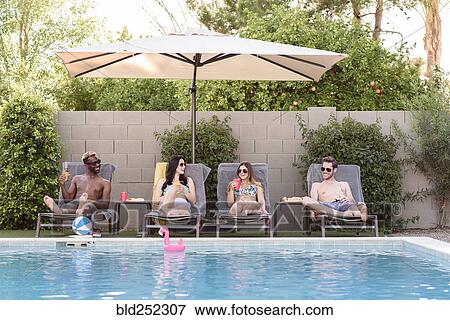 Stock Photo - Smiling friends relaxing and drinking poolside. Fotosearch