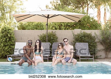 Stock Photo - Smiling friends sitting and relaxing poolside. Fotosearch