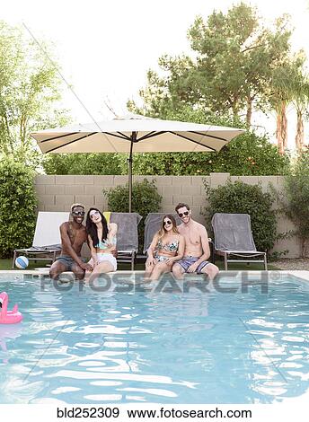 Stock Photo - Smiling friends sitting and relaxing poolside. Fotosearch
