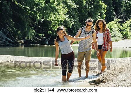 Picture - Smiling friends wading in river. Fotosearch