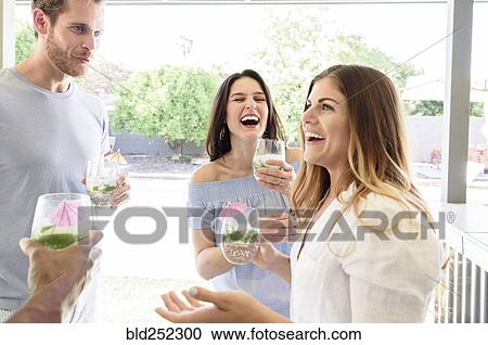 Stock Image - Smiling friends with cold drinks laughing outdoors. Fotosearch