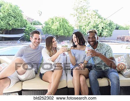 Stock Image - Smiling friends with cold drinks toasting outdoors. Fotosearch
