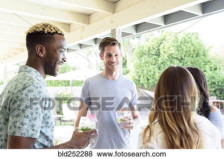 Stock Photo - Smiling friends with cold drinks talking outdoors. Fotosearch