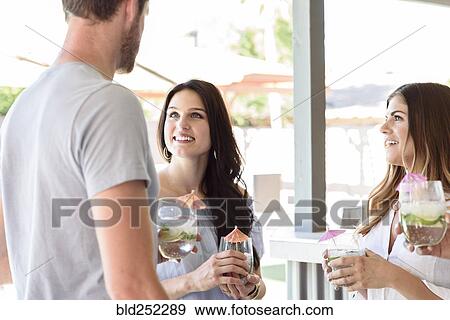 Stock Photo - Smiling friends with cold drinks talking outdoors. Fotosearch