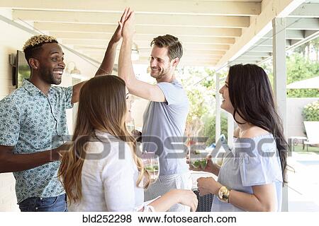 Stock Photo - Smiling friends with cold drinks high-fiving outdoors. Fotosearch