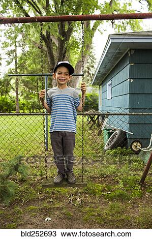 Stock Image - Smiling mixed race boy standing on backyard swing. Fotosearch