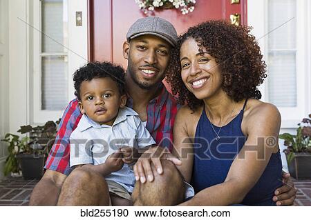 Stock Image - Smiling mixed race couple sitting on front stoop with son. Fotosearch