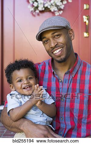 Picture - Smiling mixed race father and baby son sitting on front stoop. Fotosearch