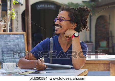 Picture - Smiling mixed race man using digital tablet at sidewalk cafe. Fotosearch