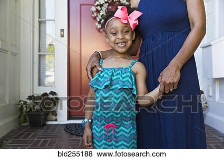 Stock Photo - Smiling mixed race mother and daughter standing on front stoop. Fotosearch