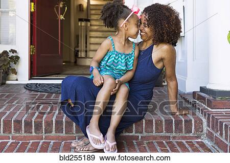 Stock Photo - Smiling mixed race mother and daughter rubbing noses on front stoop. Fotosearch