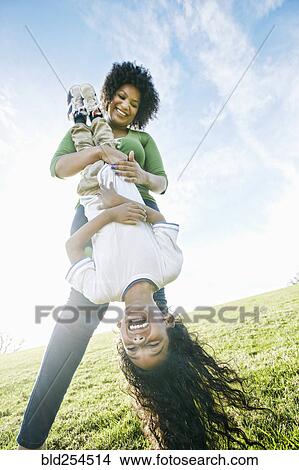 Picture - Smiling mixed race mother holding daughter upside-down. Fotosearch