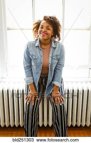 Stock Image - Smiling mixed race woman sitting on radiator. Fotosearch