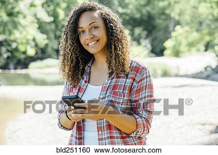 Stock Image - Smiling mixed race woman texting on cell phone outdoors. Fotosearch