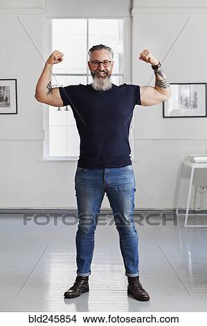 Smiling muscular Caucasian hipster man flexing biceps View Large Photo Image Picture - Smiling muscular Caucasian hipster man flexing biceps. Fotosearch