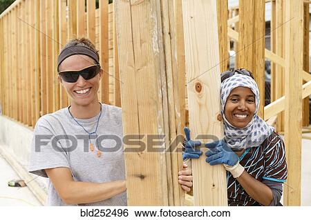 Stock Photograph - Smiling volunteers holding lumber at construction site. Fotosearch