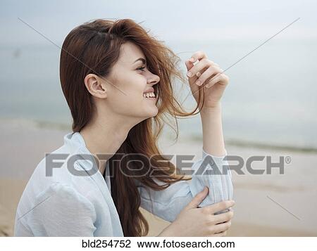 Smiling woman holding hair sitting on beach View Large Photo Image Stock Image - Smiling woman holding hair sitting on beach. Fotosearch