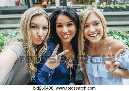 Stock Photo - Smiling women posing and gesturing for cell phone selfie. Fotosearch