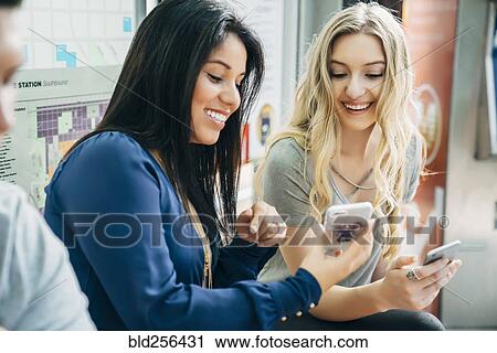 Smiling women texting on cell phones at train station View Large Photo Image Stock Image - Smiling women texting on cell phones at train station. Fotosearch