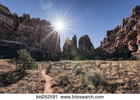 Stock Image - "Sun in blue sky over desert path, Moab, Utah, United States". Fotosearch