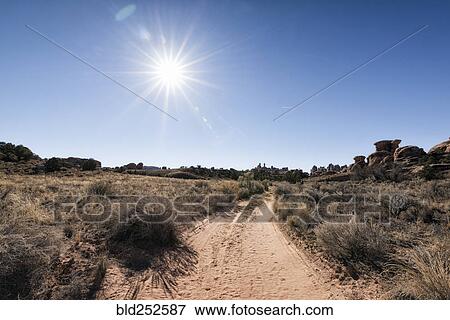 Stock Photo - "Sun in blue sky over desert path, Moab, Utah, United States". Fotosearch