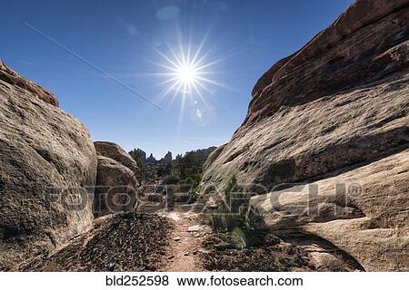 Stock Photo - "Sun in blue sky over desert path, Moab, Utah, United States". Fotosearch