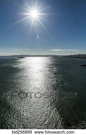 Stock Photo - Sunbeams in blue sky over bay. Fotosearch