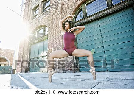 Stock Image - Sunbeams on mixed race woman dancing in city. Fotosearch