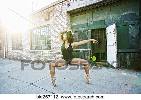 Stock Image - Sunbeams on mixed race woman dancing in city. Fotosearch