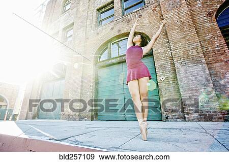 Stock Photo - Sunbeams on mixed race woman dancing in city. Fotosearch