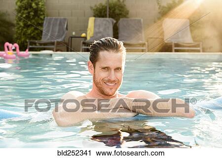 Stock Image - Sunbeams on smiling Caucasian man in swimming pool. Fotosearch