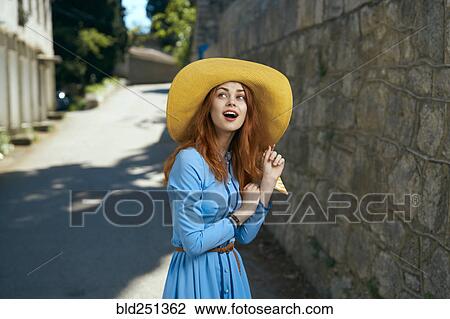 Stock Image - Surprised Caucasian woman wearing hat near stone wall. Fotosearch