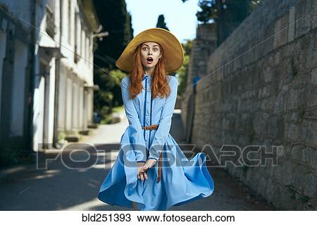 Stock Image - Surprised Caucasian woman wearing hat near stone wall. Fotosearch
