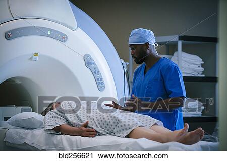 Stock Image - Technician talking to patient at scanner. Fotosearch