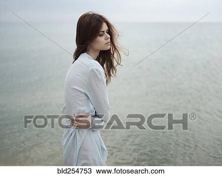 Stock Image - Troubled Caucasian woman standing near ocean. Fotosearch