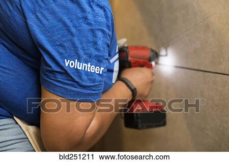 Stock Image - Volunteer black woman drilling wall. Fotosearch