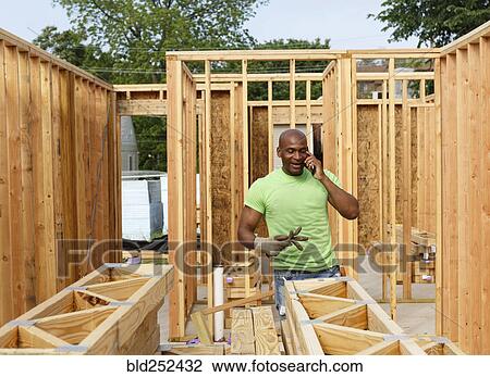 Stock Image - Volunteer building house talking on cell phone. Fotosearch