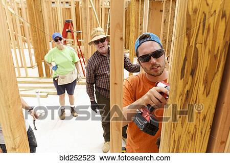 Stock Image - Volunteer using drill at construction site. Fotosearch