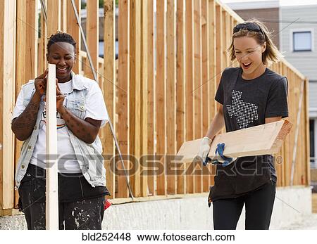 Stock Photo - Volunteers carrying lumber at a construction site. Fotosearch
