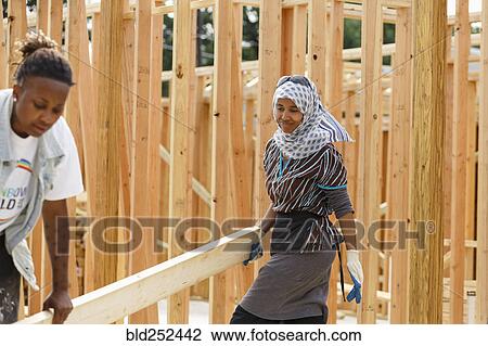 Stock Image - Volunteers carrying lumber at construction site. Fotosearch