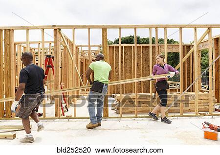 Stock Image - Volunteers carrying lumber at construction site. Fotosearch