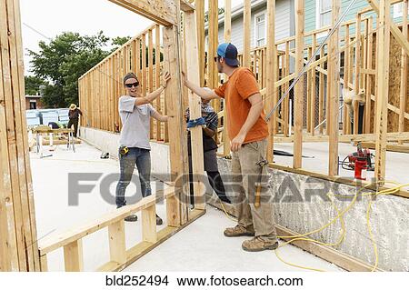 Picture - Volunteers holding framed wall at construction site. Fotosearch