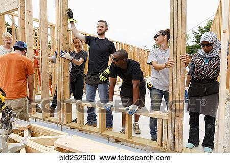 Volunteers holding framed wall at construction site View Large Photo Image Stock Image - Volunteers holding framed wall at construction site. Fotosearch