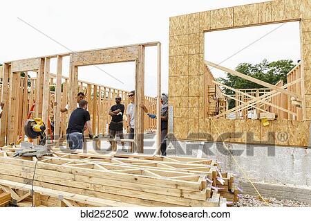 Volunteers holding framed wall at construction site View Large Photo Image Stock Image - Volunteers holding framed wall at construction site. Fotosearch